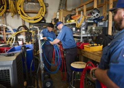 Two technicians in blue uniforms working with equipment in a cluttered workshop